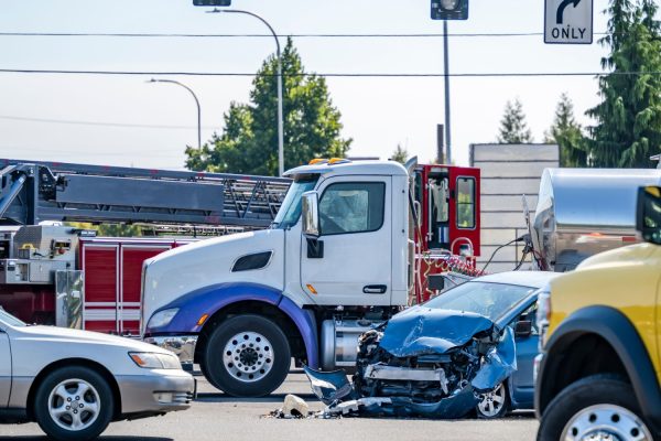 Damaged cars after a car accident crash involving a big rig semi truck with semi trailer at a city street crossroad intersection with traffic light and rescue services to help the injured