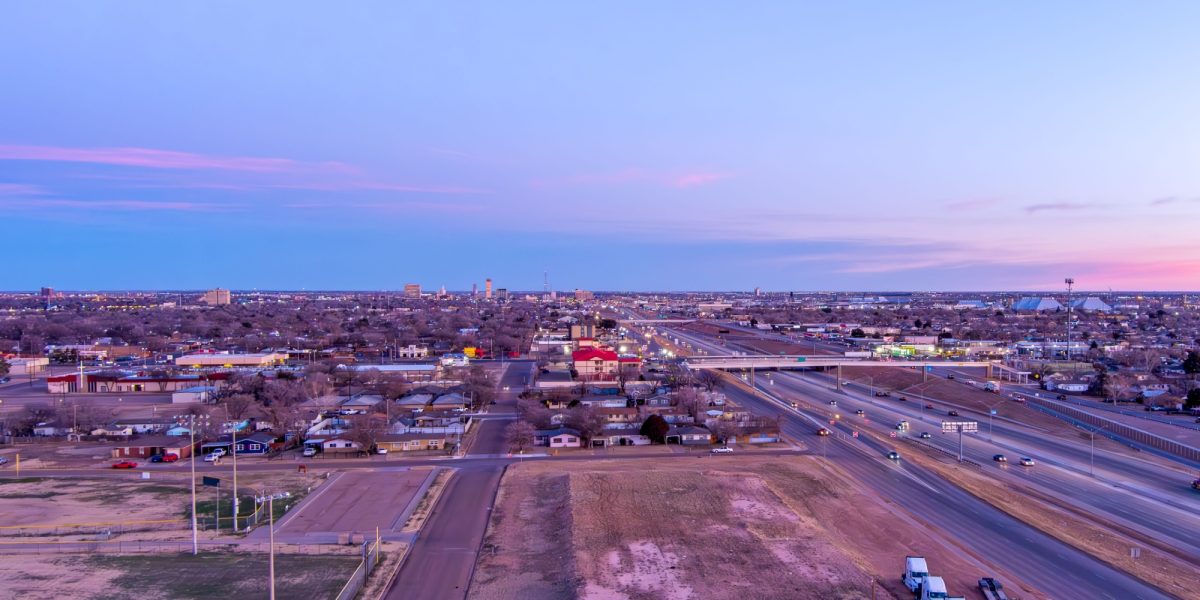 Aerial Cityscape of Lubbock Texas with traffic on the roads and tall buildings in the background against a blue sky at sunrise.