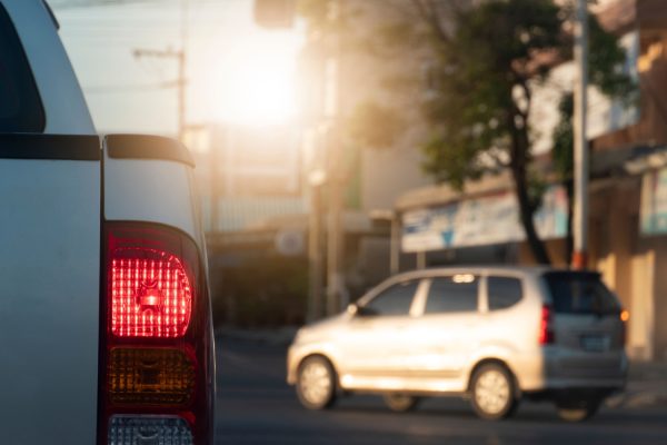 Beside of pick-up silver car brake on the road with turn light. The front with red light traffic control and blur of passing car and city.