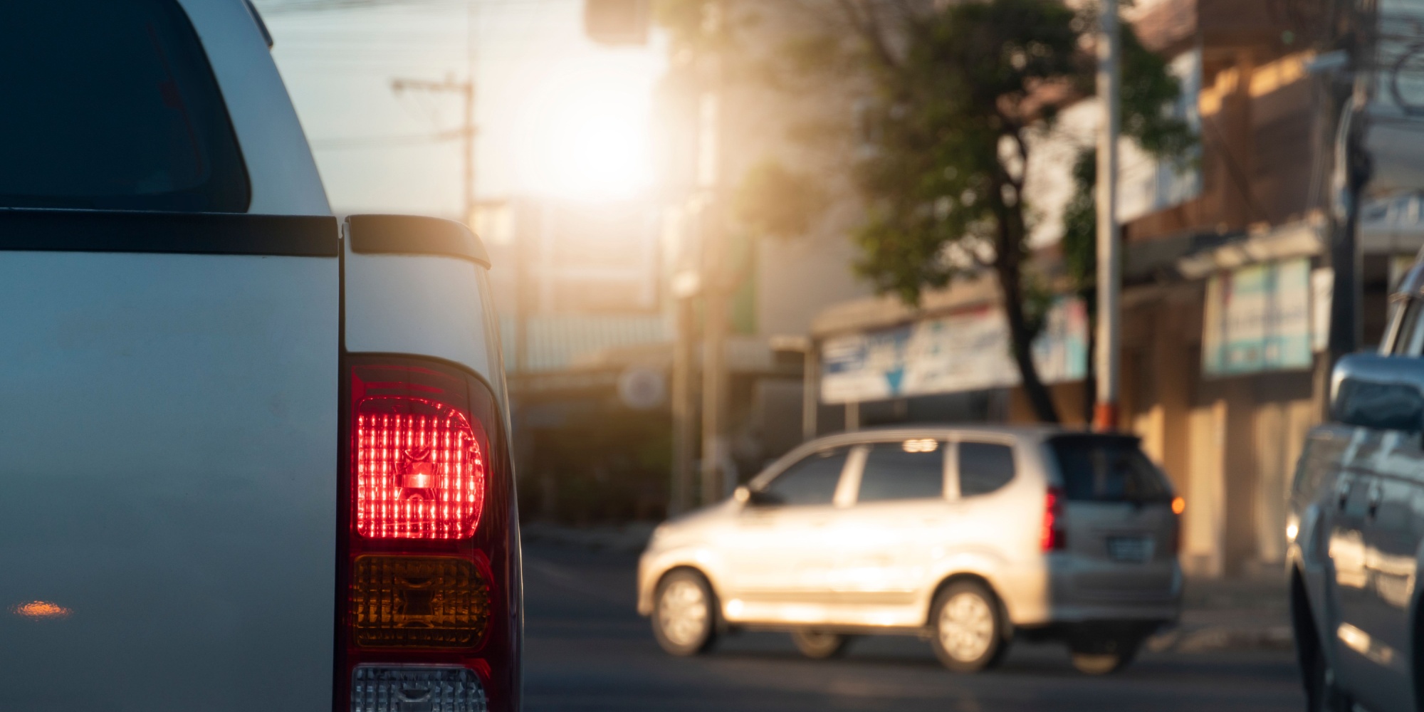 Beside of pick-up silver car brake on the road with turn light. The front with red light traffic control and blur of passing car and city.