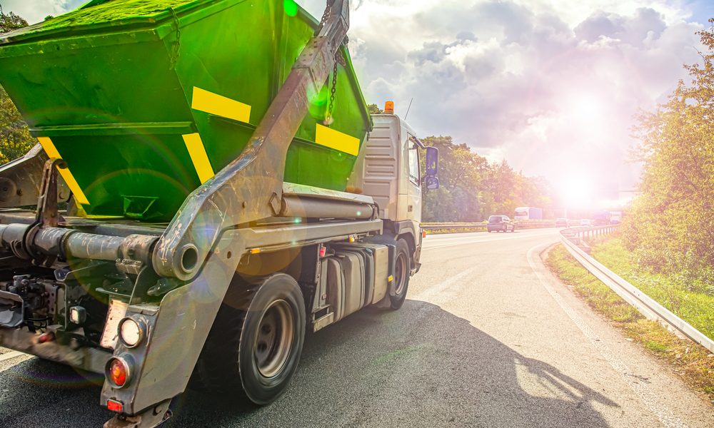 $8.5 Million Settlement for Worker Killed in Dump Truck Accident | A grey dump truck with a green container in its bed driving down a road.